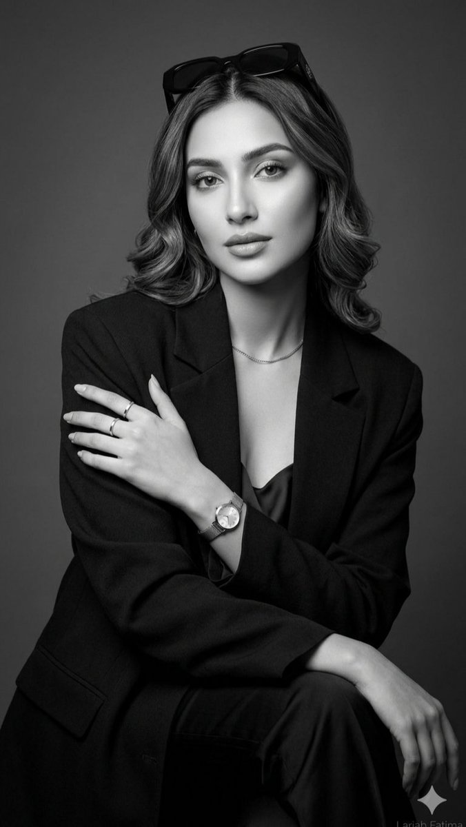 一张精致的黑白摄影棚人像照,画面中是一位举止从容优雅的年轻女性。她身穿剪裁考究的黑色西装外套,内搭丝绸吊带背心,头顶时尚地架着一副深色太阳镜。…, 图片 1