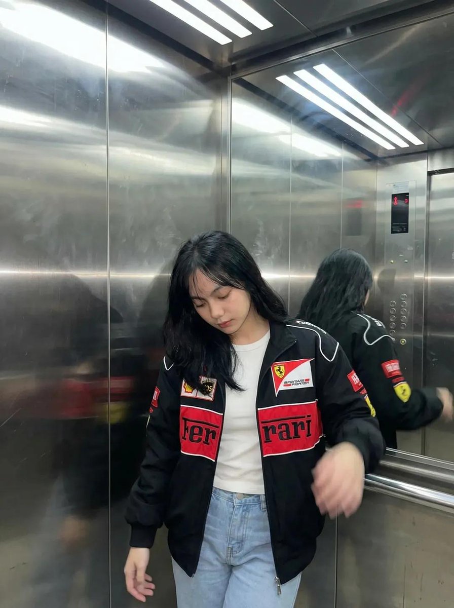 一张超写实的照片：一位年轻女性深夜坐在一间温馨的咖啡馆里，侧着头靠在自己放在木质桌面上的手臂上。她穿着一件红黑配色的赛车风格夹克。表情平静、略…, 图片 2