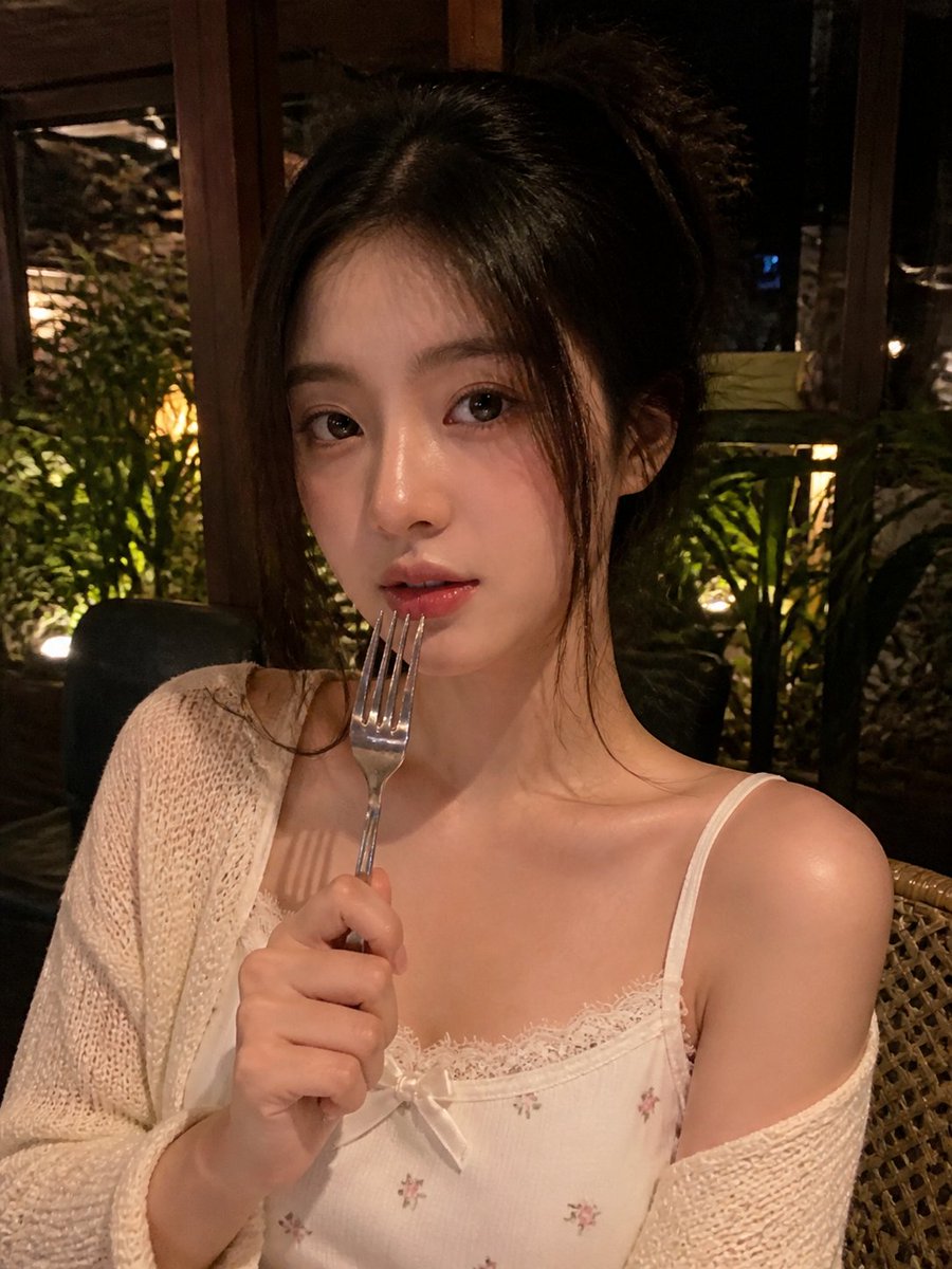 一张写实风格的弱光手机人像照片,主体是一位年轻成年女性,夜晚坐在一家温馨的咖啡馆或餐厅内。近景半身构图,画面比例约为 4:5 或接近正方形。相…, 图片 1