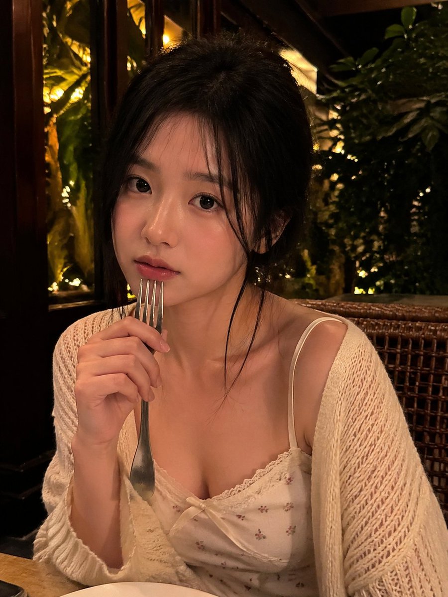 一张写实风格的弱光手机人像照片,主体是一位年轻成年女性,夜晚坐在一家温馨的咖啡馆或餐厅内。近景半身构图,画面比例约为 4:5 或接近正方形。相…, 图片 2