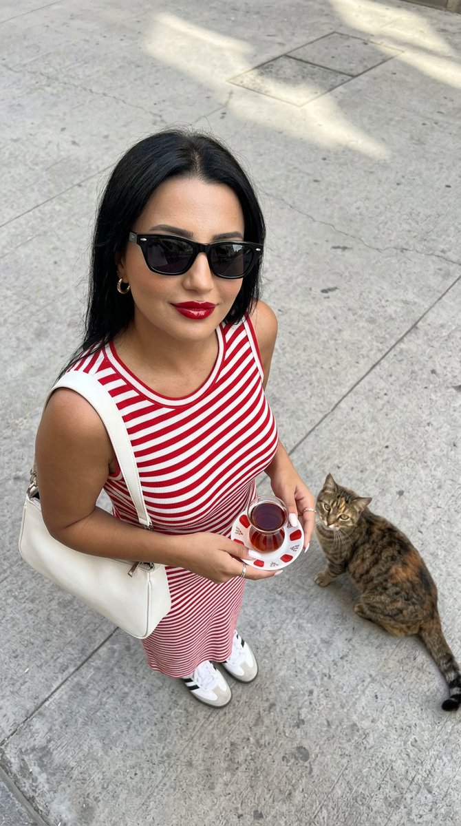 一张高角度俯视的超写实时尚摄影照片：一位时尚年轻女性站立在干净浅灰色的水泥街道上，自信而有魅力地抬头直视镜头。她留着没有头巾的深色长发，唇色为…, 图片 1