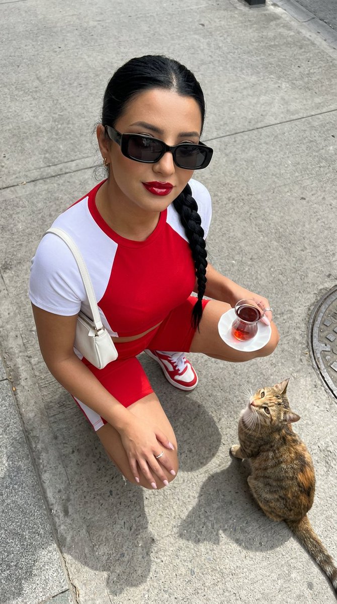 一张高角度俯视的超写实时尚摄影照片：一位时尚年轻女性站立在干净浅灰色的水泥街道上，自信而有魅力地抬头直视镜头。她留着没有头巾的深色长发，唇色为…, 图片 2
