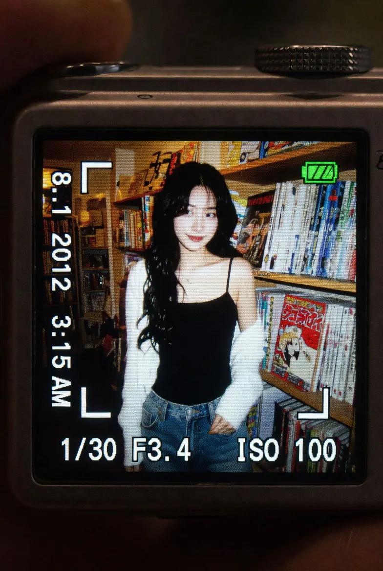 一个真实感的特写镜头,拍摄的是在昏暗室内环境中明亮发光的一台小型数码相机屏幕。LCD 屏幕上显示着一张抓拍风格的早期 2010 年代风格照片,…, 图片 2