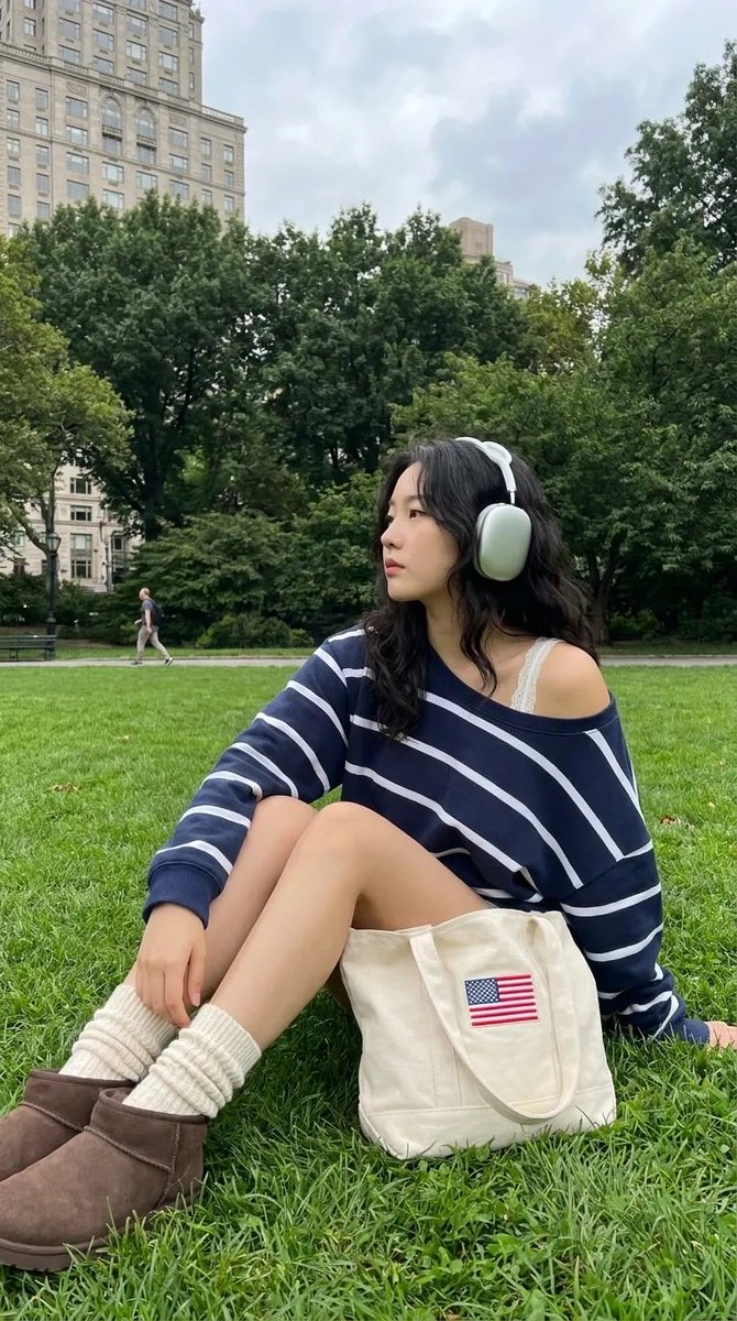 中景全身镜头：一位时髦的24岁韩国女性在像中央公园这样的知名城市公园的翠绿草坪上放松休憩。她弯曲膝盖坐着，身体微微后倾，姿态放松，同时转头看向…, 图片 1