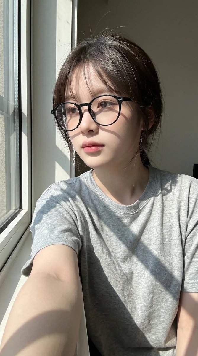 超写实抓拍式智能手机自拍照肖像：一位年轻东亚女性室内坐在一扇大窗户旁，处于明亮的自然日光下。保持与上传的面部参考高度相似的面部特征：柔和的椭圆…, 图片 1
