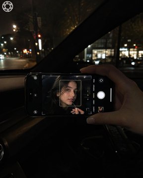 照片于夜间在车内拍摄；画面中仅露出一只女性的手和一部iPhone，年轻女性的面部仅出现在手机屏幕上。相机位于副驾驶侧，构图同时纳入挡风玻璃与手…, 图片 1
