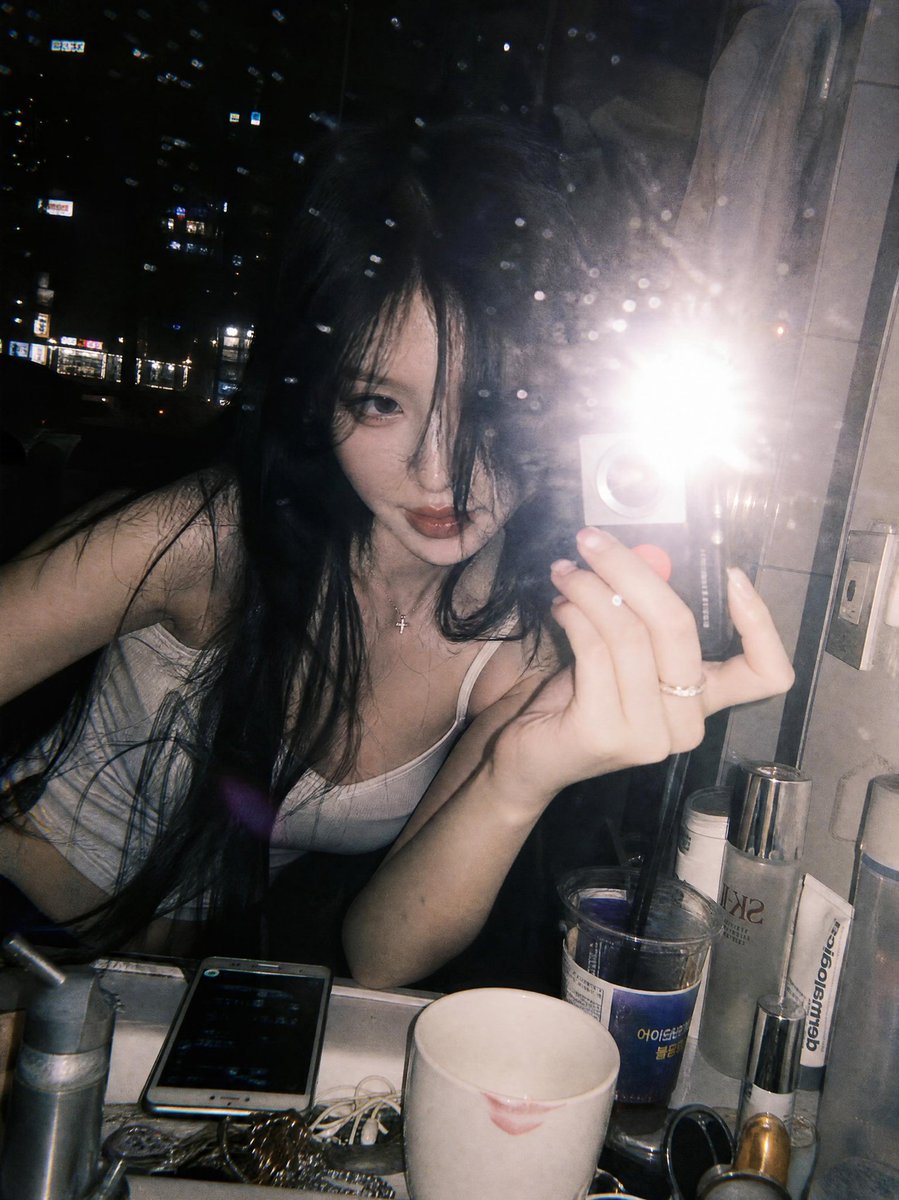 一张氛围感十足的深夜镜面自拍，拍摄于一间俯瞰璀璨城市天际线的豪华高层公寓浴室中。一位年轻女性留着略带凌乱黑色长发，身体向前倚靠在白色大理石洗手…, 图片 2