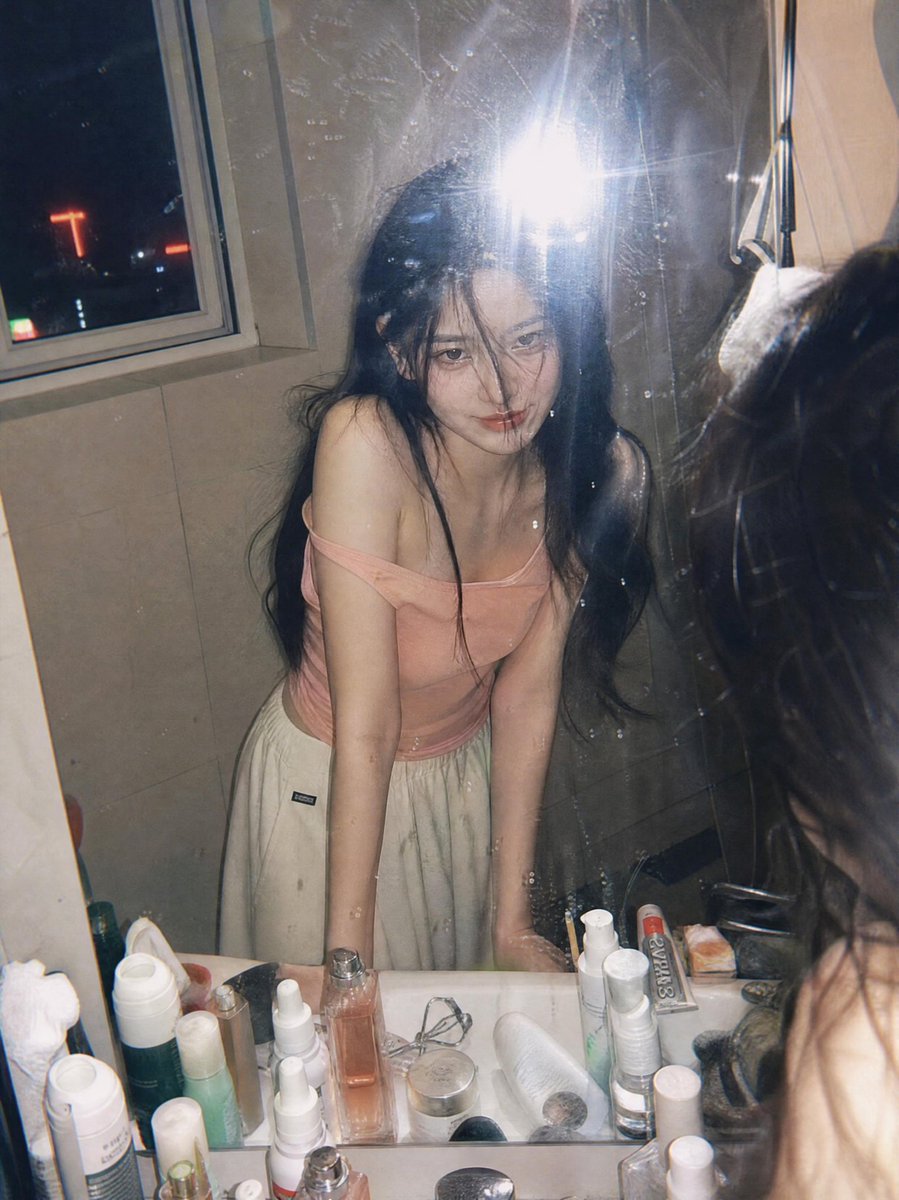超写实抓拍胶片摄影人像：一位年轻女子夜晚俯身在浴室洗手台前，透过镜子凝视自己。画面通过一面略有污渍的镜子拍摄，呈现自然的反射与细腻的瑕疵。她留…, 图片 1