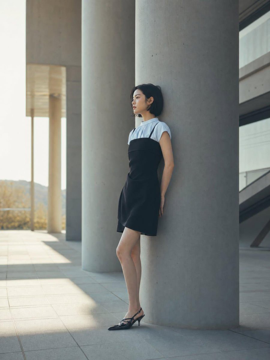 一位身材纤细的年轻女性,留着黑色短波波头发型,靠在现代建筑广场上一根巨大的混凝土柱上,身穿黑色吊带裙内搭白色短袖上衣,脚踩黑色尖头后跟凉鞋,妆…, 图片 1