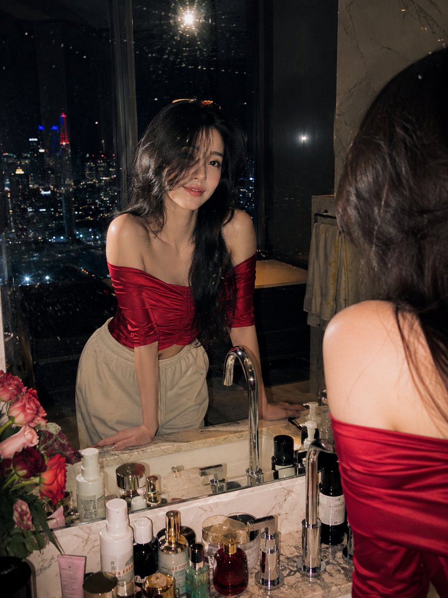 超写实电影感夜景人像摄影:一位美丽的年轻女子站在顶层豪宅豪华大理石浴室梳妆台前,俯瞰夜晚璀璨的城市天际线。她身穿酒红色光泽缎面露肩上衣,面料垂…, 图片 1