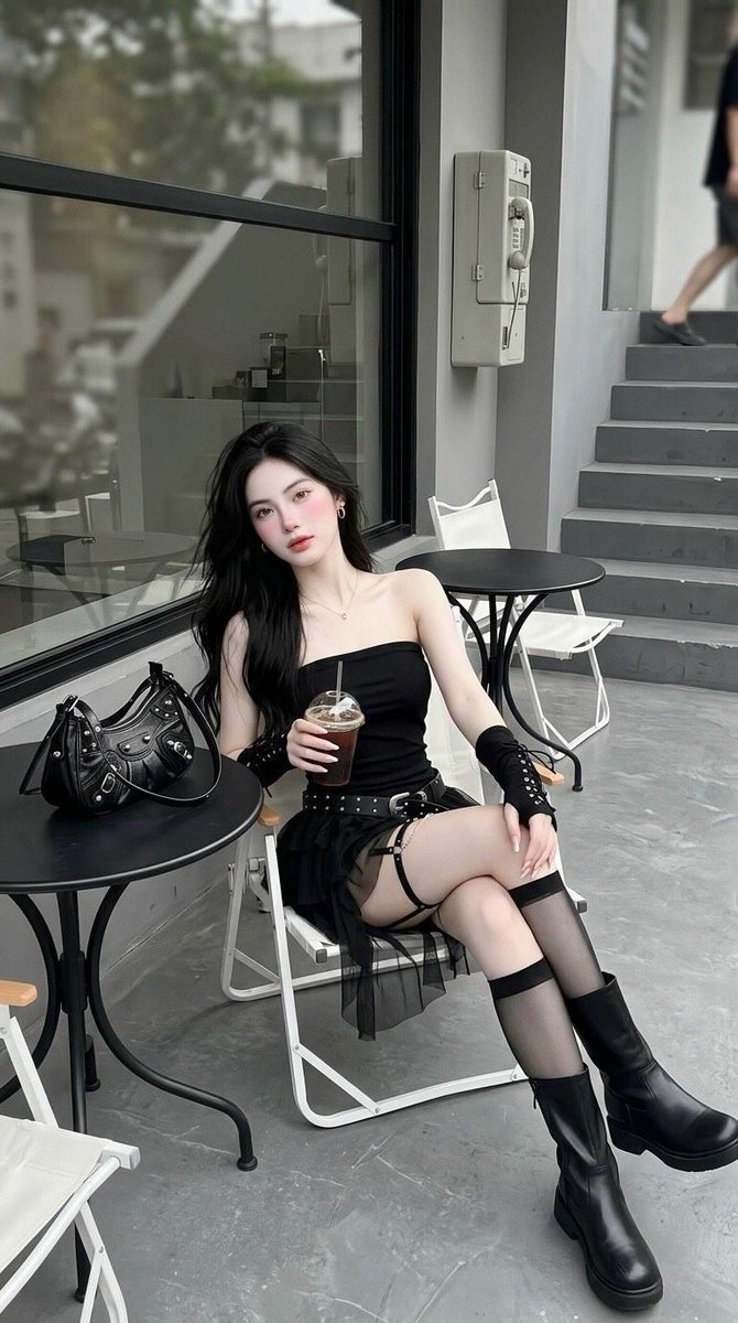 户外极简风格咖啡馆中,一位年轻女性的全身照片:长直黑发,坐在白色折叠椅上,身穿黑色抹胸迷你连衣裙、镶钉宽腰带、黑色无指系带护臂、大腿吊袜带、透…, 图片 1