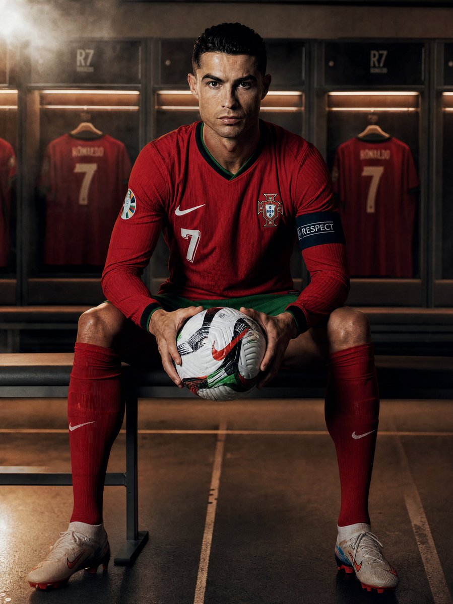 创作一张超写实的摄影作品：[team]球队的[footballer]坐在更衣室里，手持一个足球，全身正面视角，目光直视镜头。球员身穿官方球队球…, 图片 1
