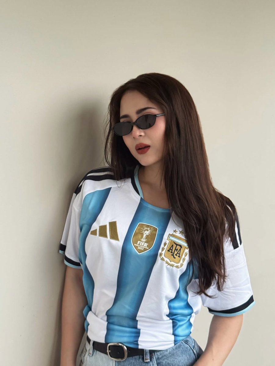 超现实风格的时尚人像摄影：一位时髦的年轻女性，身穿不同国家队的足球球衣（阿根廷、葡萄牙、巴西），在室内一面干净极简的米白色墙壁前自信地摆姿势。…, 图片 1