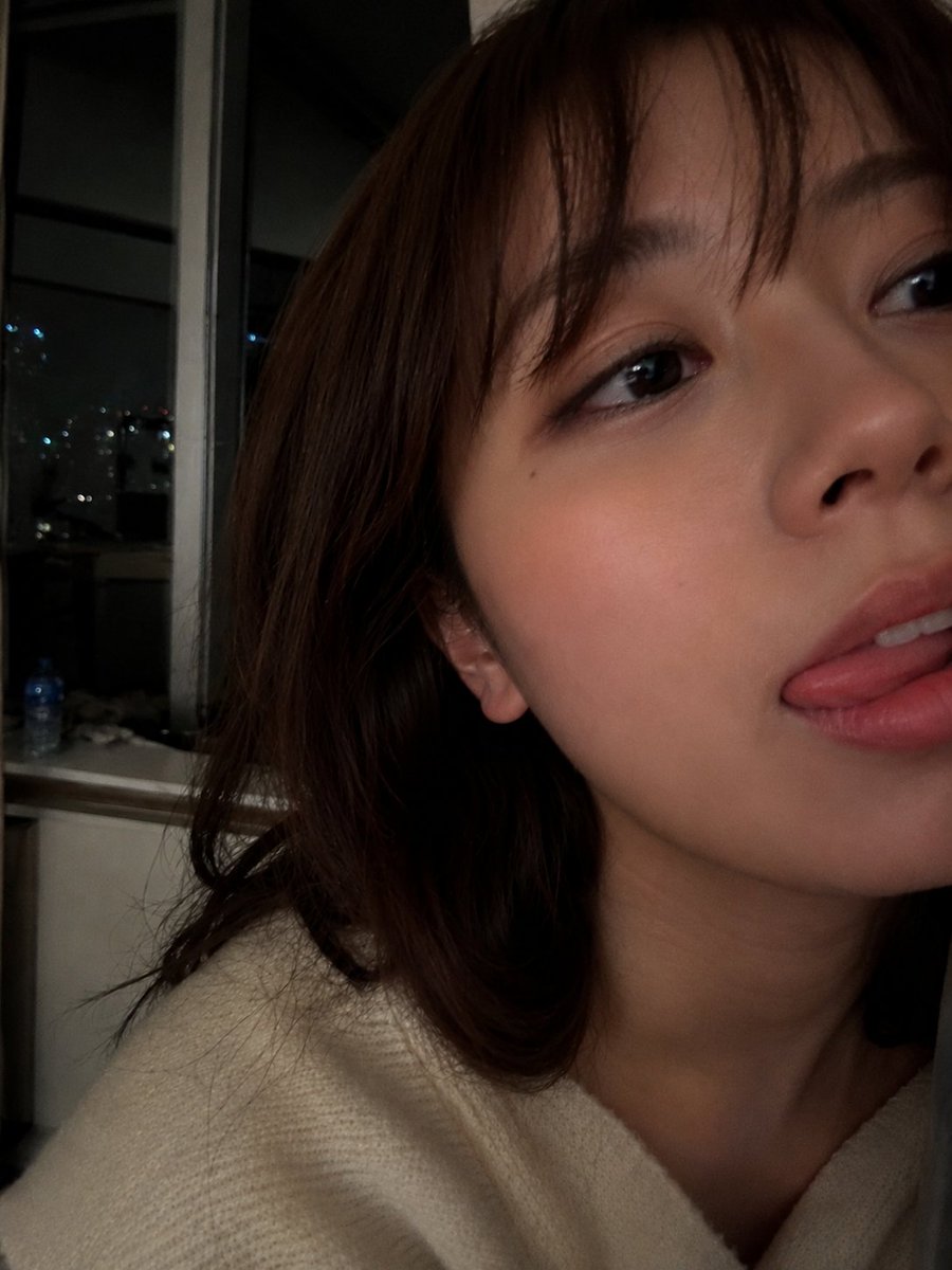 室内夜景中，使用智能手机摄像头拍摄的年轻女性超写实特写自拍肖像。肌肤柔和自然，肤质光滑细腻，双颊微微泛红，嘴唇粉嫩水润，表情俏皮，舌头轻触上唇…, 图片 1