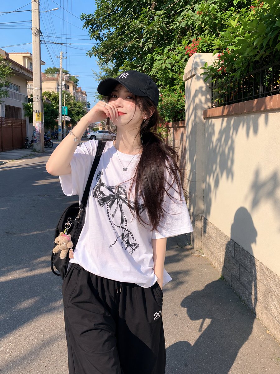 年轻漂亮的日本女孩,肤色白皙,妆容自然柔和,长长的深色头发在黑色棒球帽下扎成低马尾,身穿宽松的白色印花T恤和黑色宽松全长运动裤。在一个晴朗的下…, 图片 1