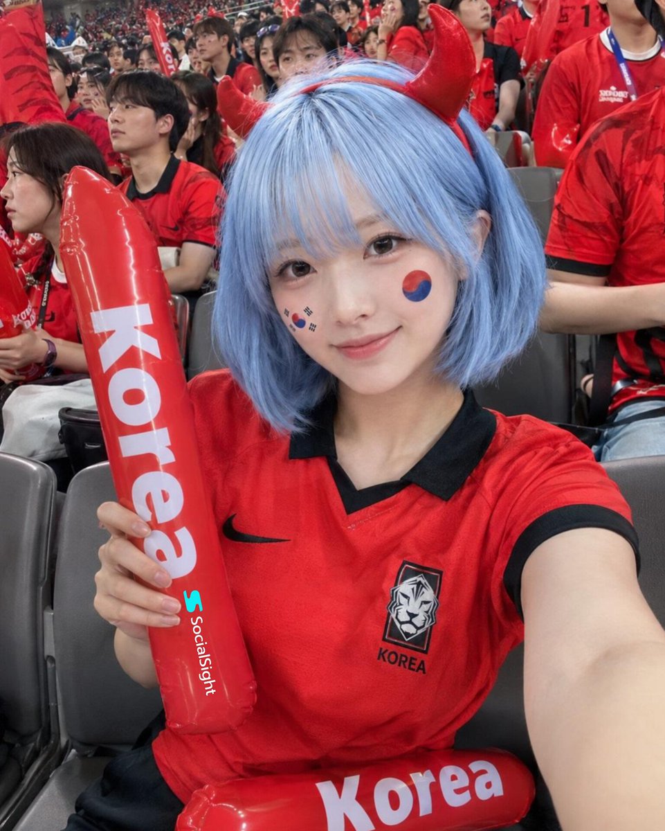 在一座座无虚席的体育场内，国际足球比赛期间，一位美丽的足球迷坐在看台上拍摄的极致写实自拍，齐耳短款粉蓝色波波头，闪亮的红色恶魔角发箍，柔和自然…, 图片 1