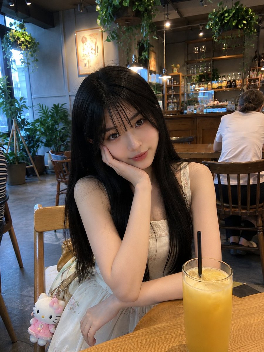 年轻的日本女孩,留着柔顺的长黑发、轻柔蓬松的刘海、白皙透亮的肌肤和一双大而传神的眼睛,随意地坐在一家温馨现代的咖啡馆里。身穿一件精致的奶油白无…, 图片 1