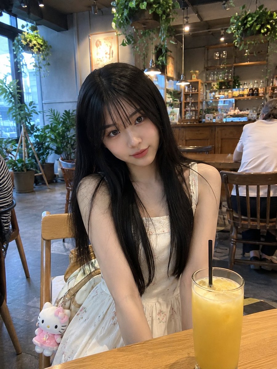 年轻的日本女孩,留着柔顺的长黑发、轻柔蓬松的刘海、白皙透亮的肌肤和一双大而传神的眼睛,随意地坐在一家温馨现代的咖啡馆里。身穿一件精致的奶油白无…, 图片 2