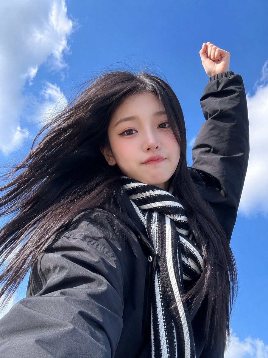 极致真实的智能手机自拍照，一位美丽的东亚年轻女性，从极具戏剧性的低角度仰拍，背景是鲜艳的蓝天和柔和的白色云朵。她拥有又长又直的乌黑长发在风中自…, 图片 2