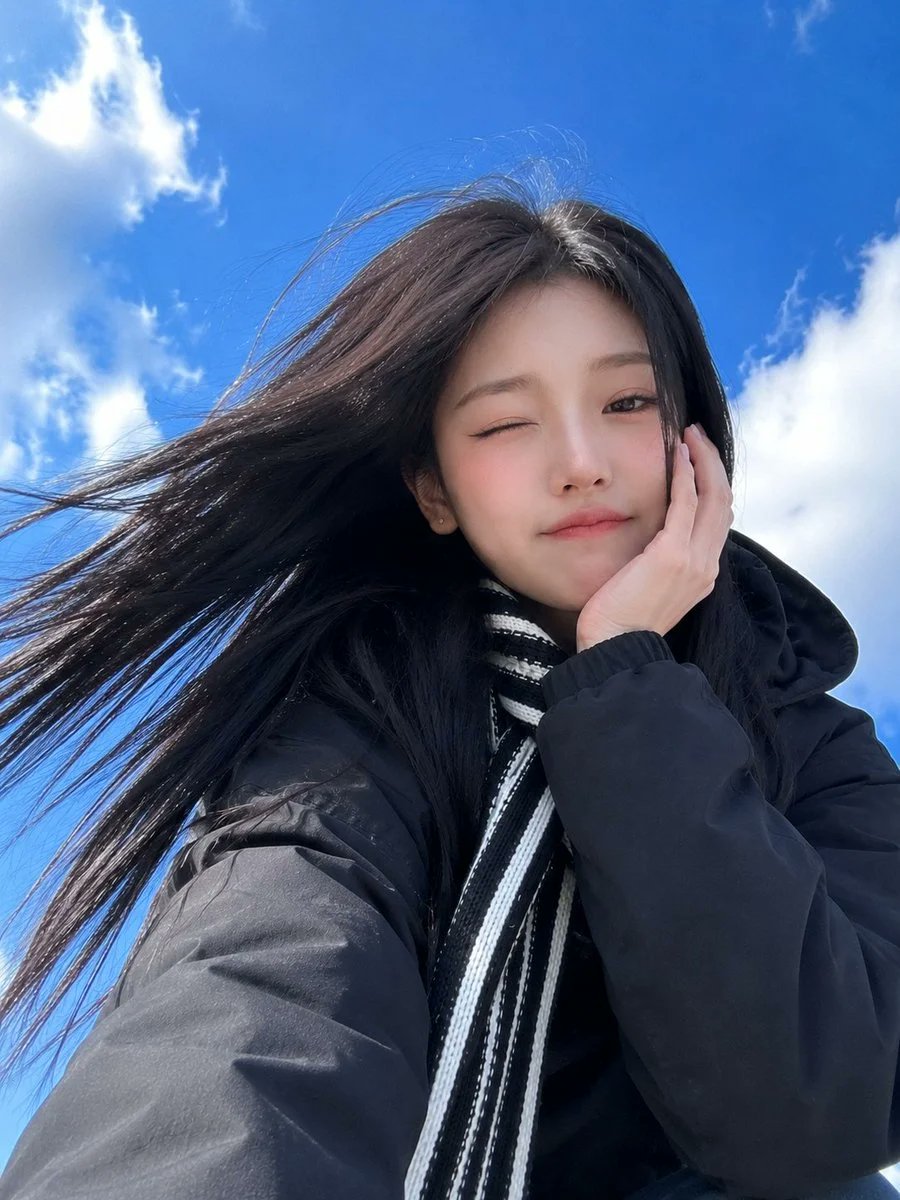 超写实智能手机自拍：一位年轻漂亮的东亚女性，以戏剧性低角度视角拍摄，背景是带有柔软白云的鲜艳蓝天。她留着顺直乌黑长发，在风中自然飘动，拥有白皙…, 图片 1