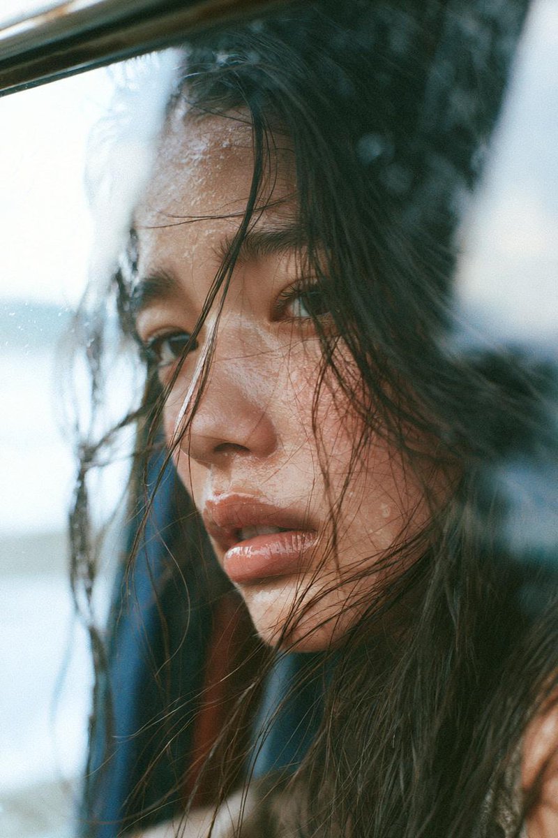 一位忧郁的年轻东亚女性,留着略显凌乱的长黑发,在黄金时刻静静坐在一扇大窗旁,柔和的阳光以温暖的电影色调照亮她的面庞。她若有所思地望向远方,妆容…, 图片 2