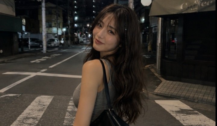 一张电影感十足的夜间街头抓拍人像,拍摄于日本街头,使用 iPhone 拍摄。一名年轻女子,长长的深棕色波浪卷发中编有一缕细辫,淡妆,嘴角带着若…, 图片 4