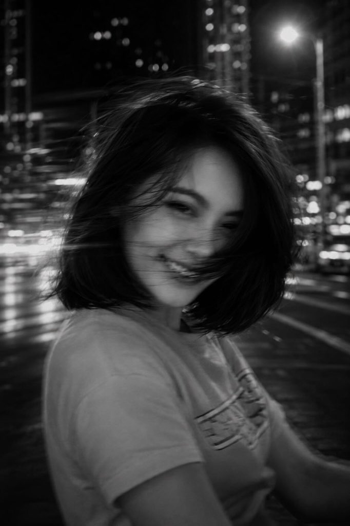一张黑白电影感的城市夜景照片，画面中一位年轻女子位于前景，略微偏离中心，正在转头过程中，长发在画面中甩动成柔和、幽灵般的发丝。长曝光拍摄，带有…, 图片 2