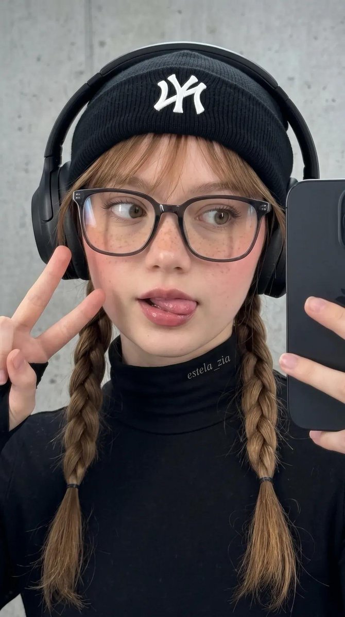 不要改变她的脸部。一张酷感都市街头风的时尚年轻女性特写自拍肖像。她身穿全黑装束,搭配修身高领上衣、带白色logo的黑色毛线帽、夸张的黑色头戴式…, 图片 2