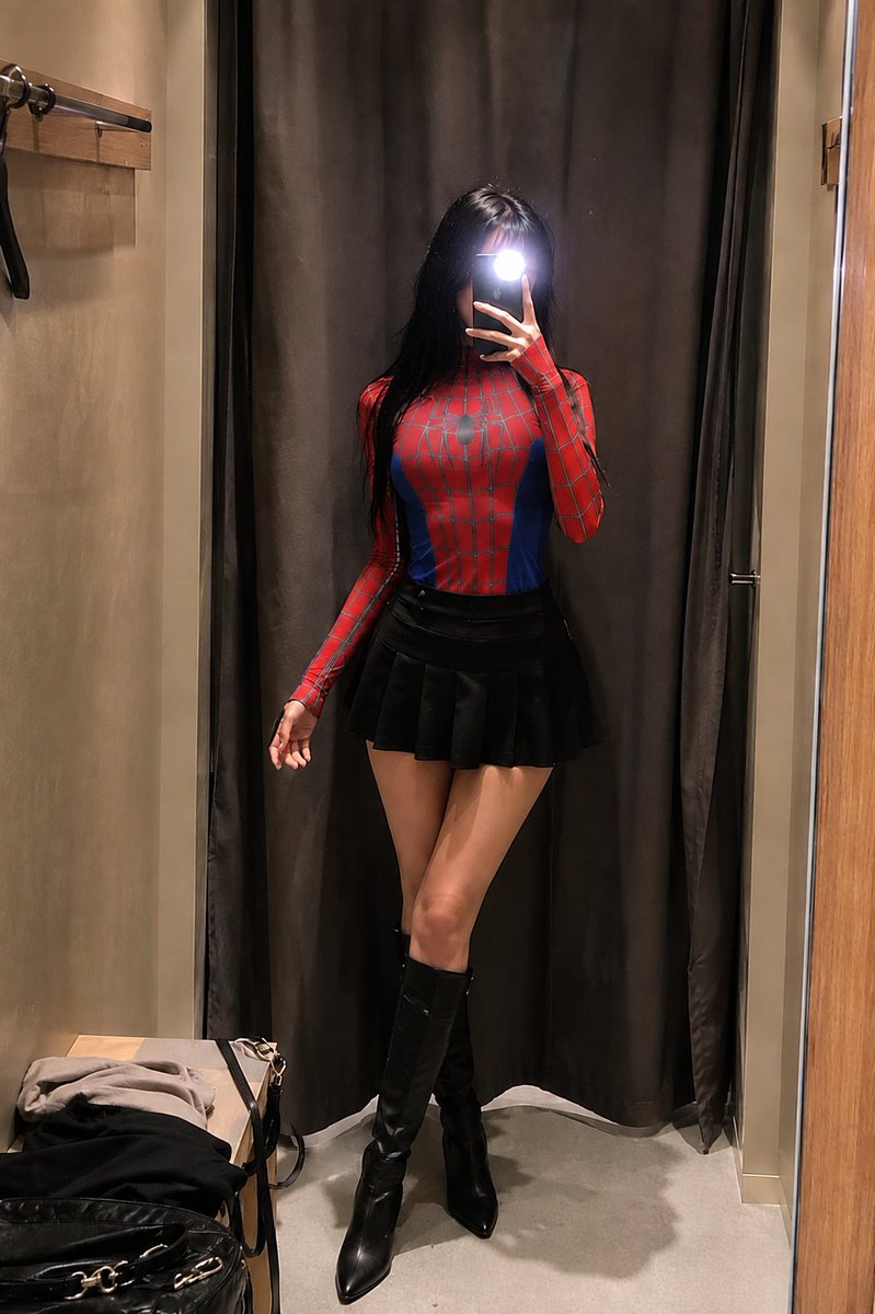 1- 一位身材纤细的年轻女性在试衣间对着镜子自拍，身穿紧身红蓝蜘蛛主题紧身连体衣（灵感来自蜘蛛侠），黑色长直发配齐刘海，手持手机闪光灯遮住面部…, 图片 1