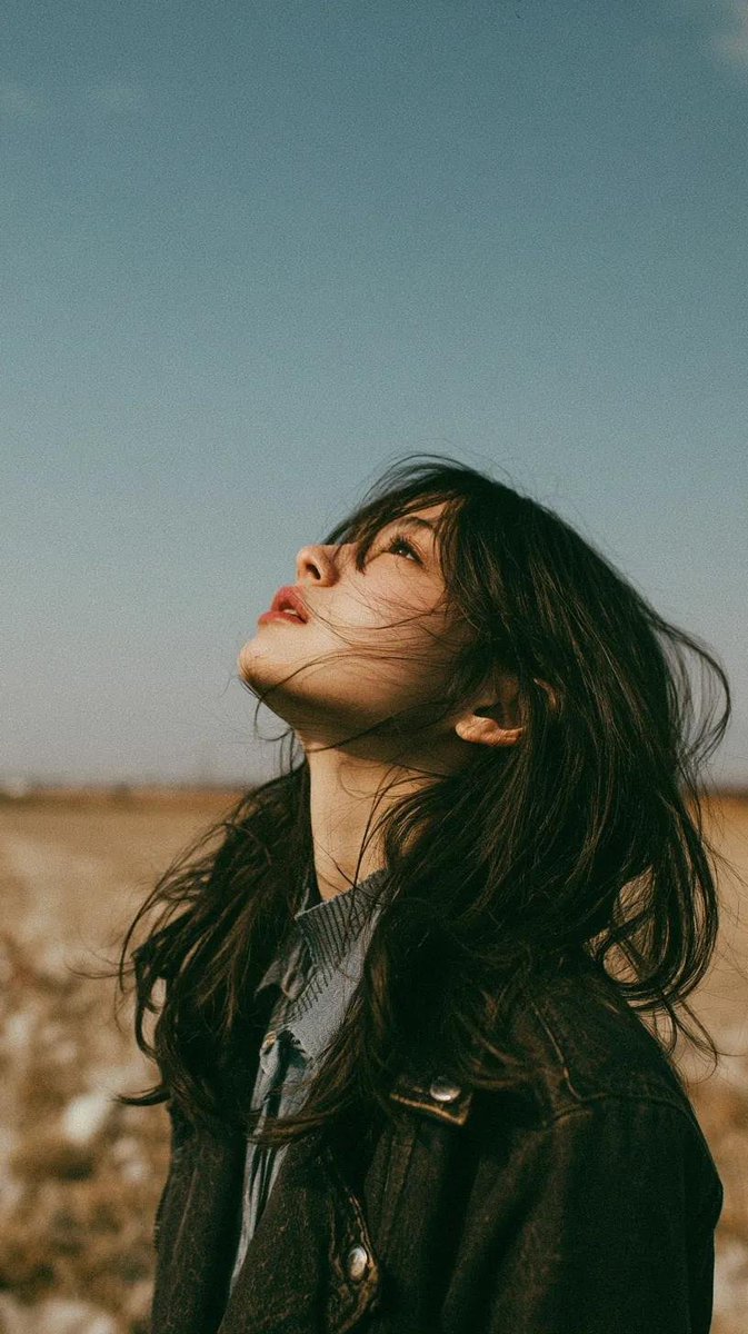 电影极简风格肖像：一位美丽的年轻东亚女性独自伫立在开阔的野花草甸上，头顶是无限的蓝天，她双眼微闭或半睁，仰望天空，仿佛在拥抱微风。乌黑长发自然…, 图片 1
