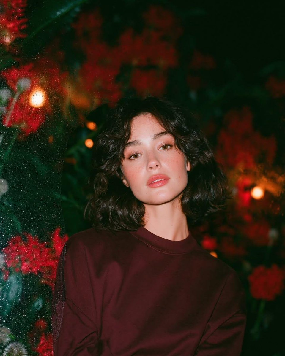 梦幻的电影感夜景人像:一位美丽的年轻女性,留着短款波浪深色头发,皮肤散发着自然光泽,身穿一件宽松的酒红色圆领卫衣,夜晚站在一座郁郁葱葱的花园中…, 图片 1