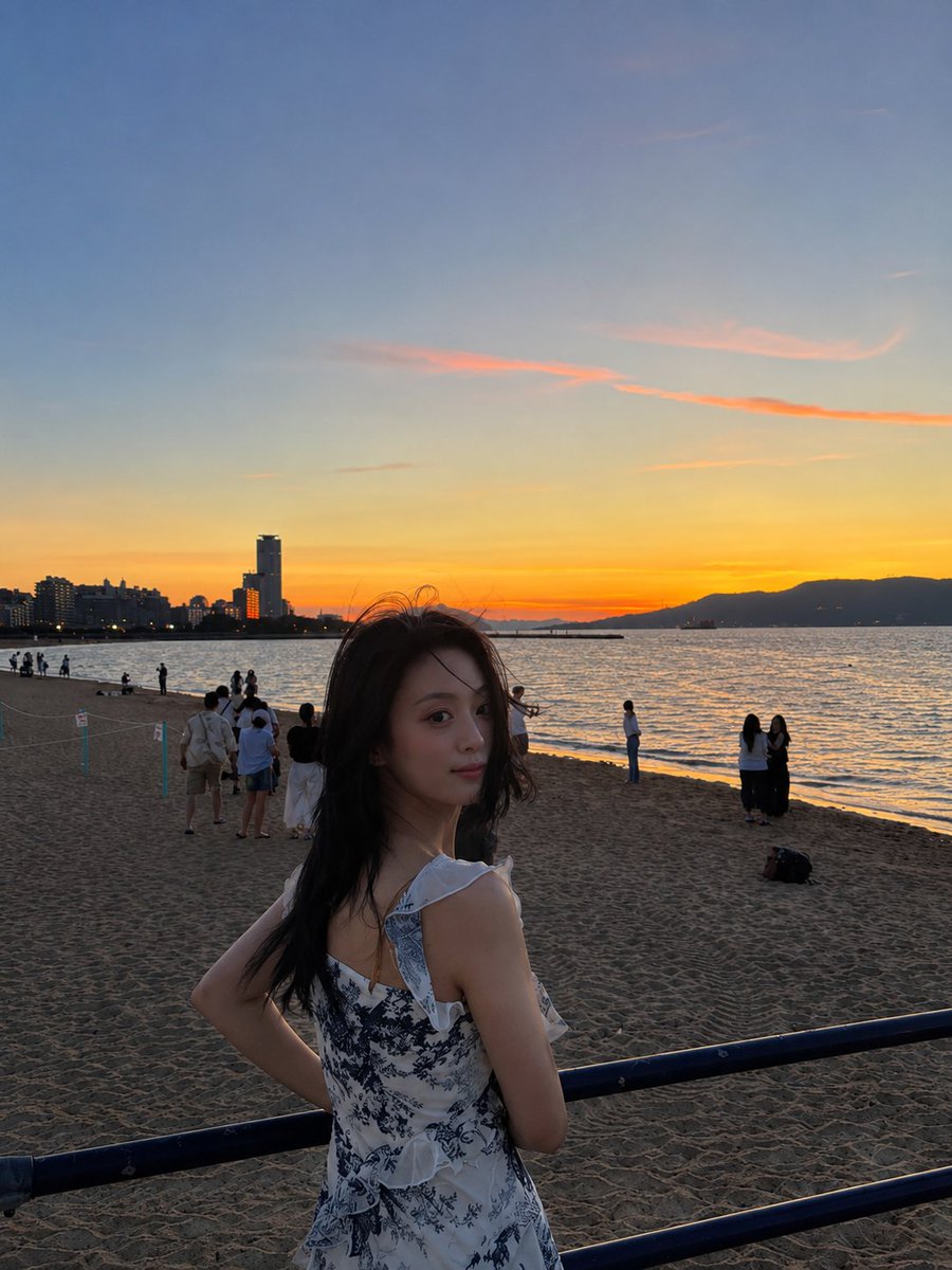超现实电影感旅行照片:一位年轻的东亚女性站在沙滩上,沐浴在令人屏息的日落中,采用竖向 3:4 构图。她身穿一件精致的白色连衣裙,点缀着细腻的蓝…, 图片 1