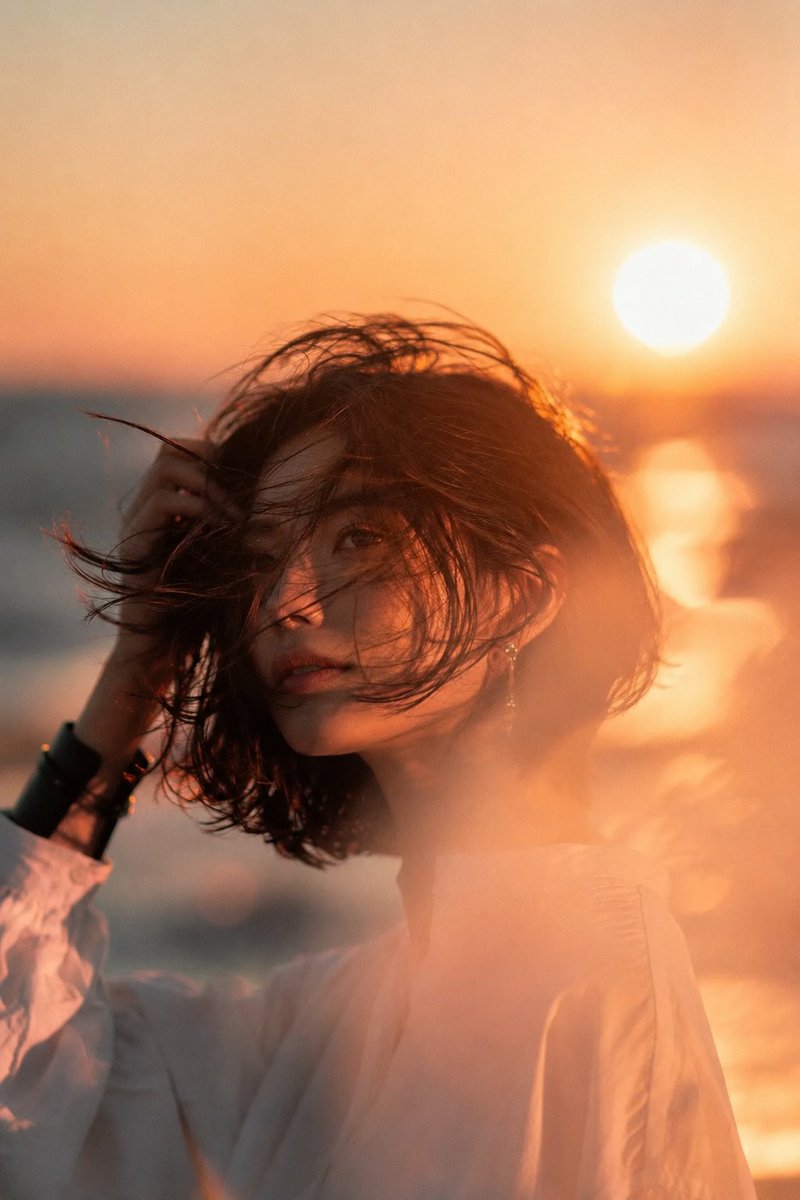 海滩日落中的美丽年轻亚洲女性,中景电影肖像。深色短发波波头在海风中飘扬,头部微向左倾,手正在整理头发。甜美浪漫的瞬间。精致优雅的耳饰,简约宽松…, 图片 1