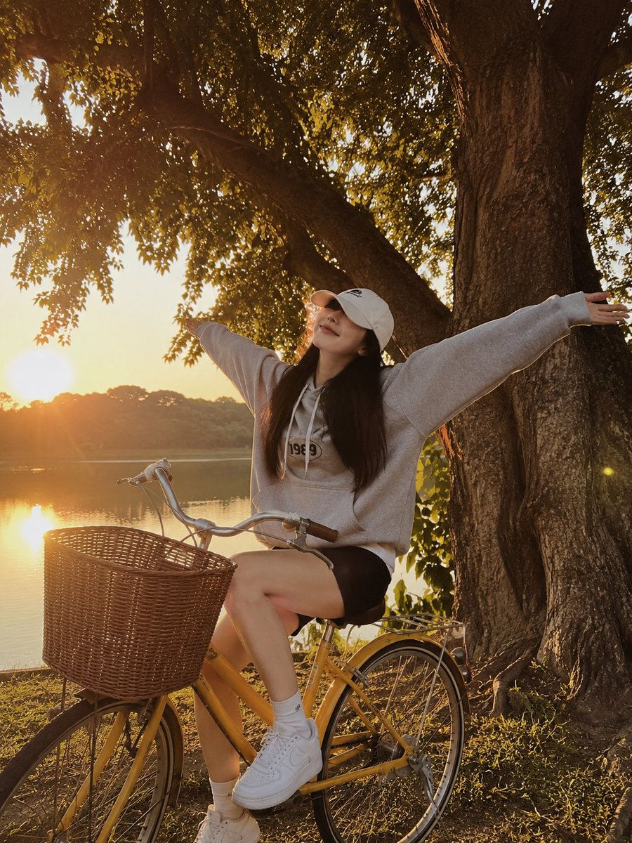 一张黄金时段的写实生活方式摄影照片，画面中一位年轻女子俏皮地坐在一辆复古黄色自行车旁，旁边是一片宁静的湖泊。她张开双臂，摆出愉悦、无忧无虑的姿…, 图片 2