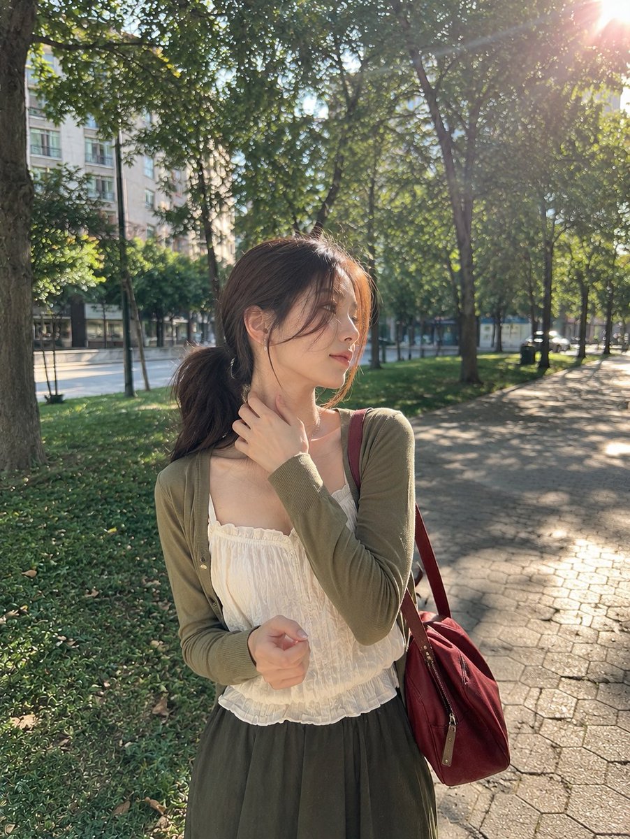 一张照片般逼真的抓拍户外肖像,画面中一位年轻女子在晴朗的午后站立于宁静的城市公园。她留着一头深棕色长发,梳成松散的低马尾,几缕纤细的碎发轻柔地…, 图片 1