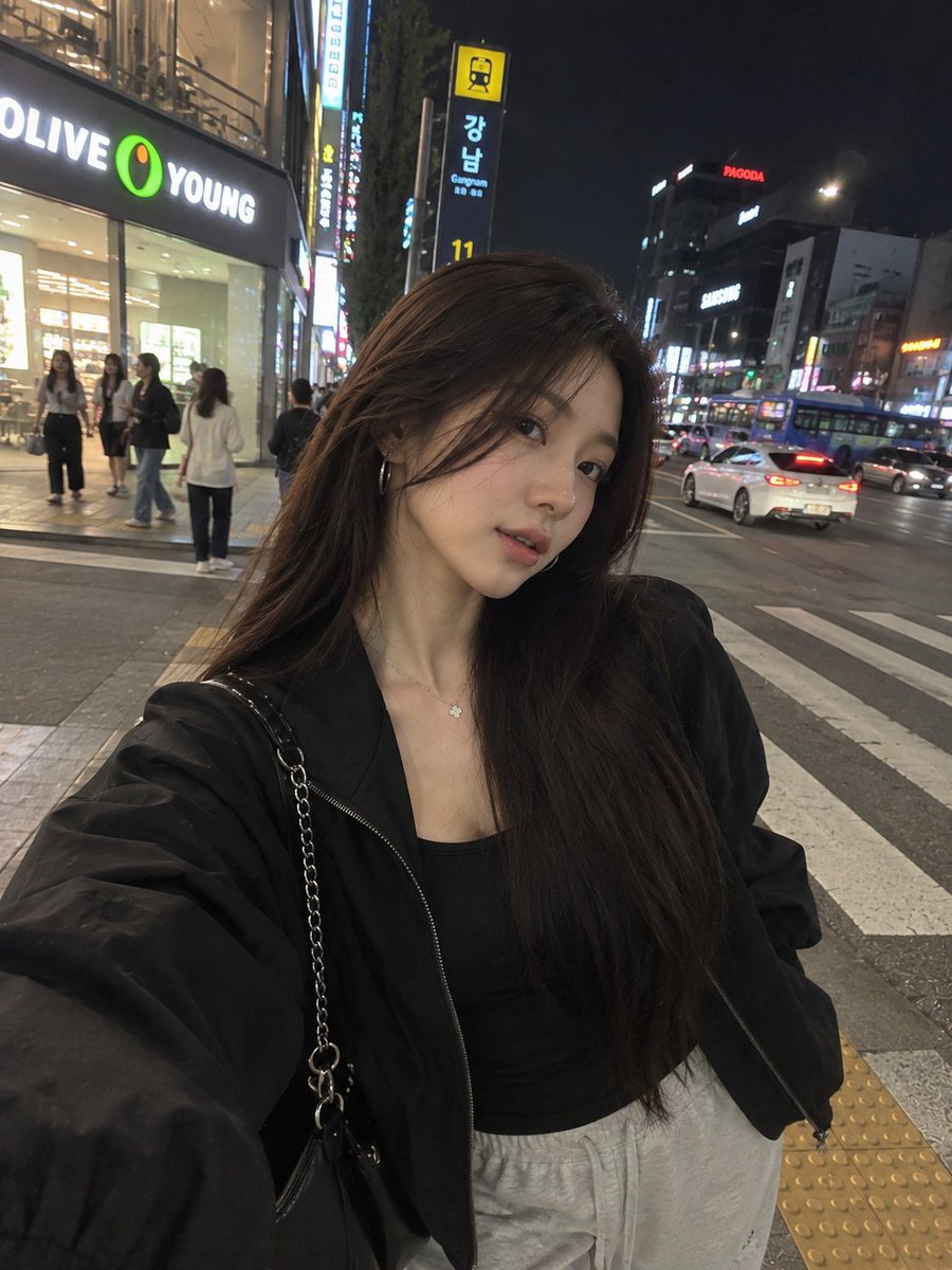 一张照片级写实风格的夜间街头人像照,一位年轻女子在繁华的韩国城市街区中随意地自拍。她留着长而顺直的黑发,妆容柔和自然,佩戴着低调的环形耳环和一…, 图片 2