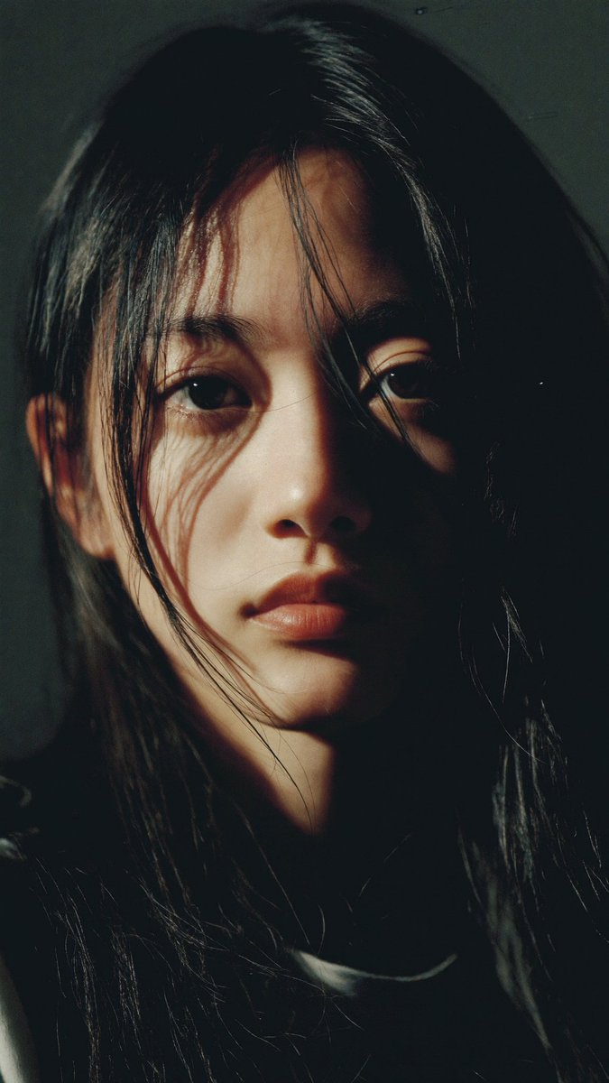特写电影感人像:一位年轻的东亚女性,长长的略带凌乱的黑发披在肩上,几缕散发拂过脸庞。她直视镜头,表情平静、专注而略带忧郁。左侧柔和而戏剧性的侧…, 图片 1