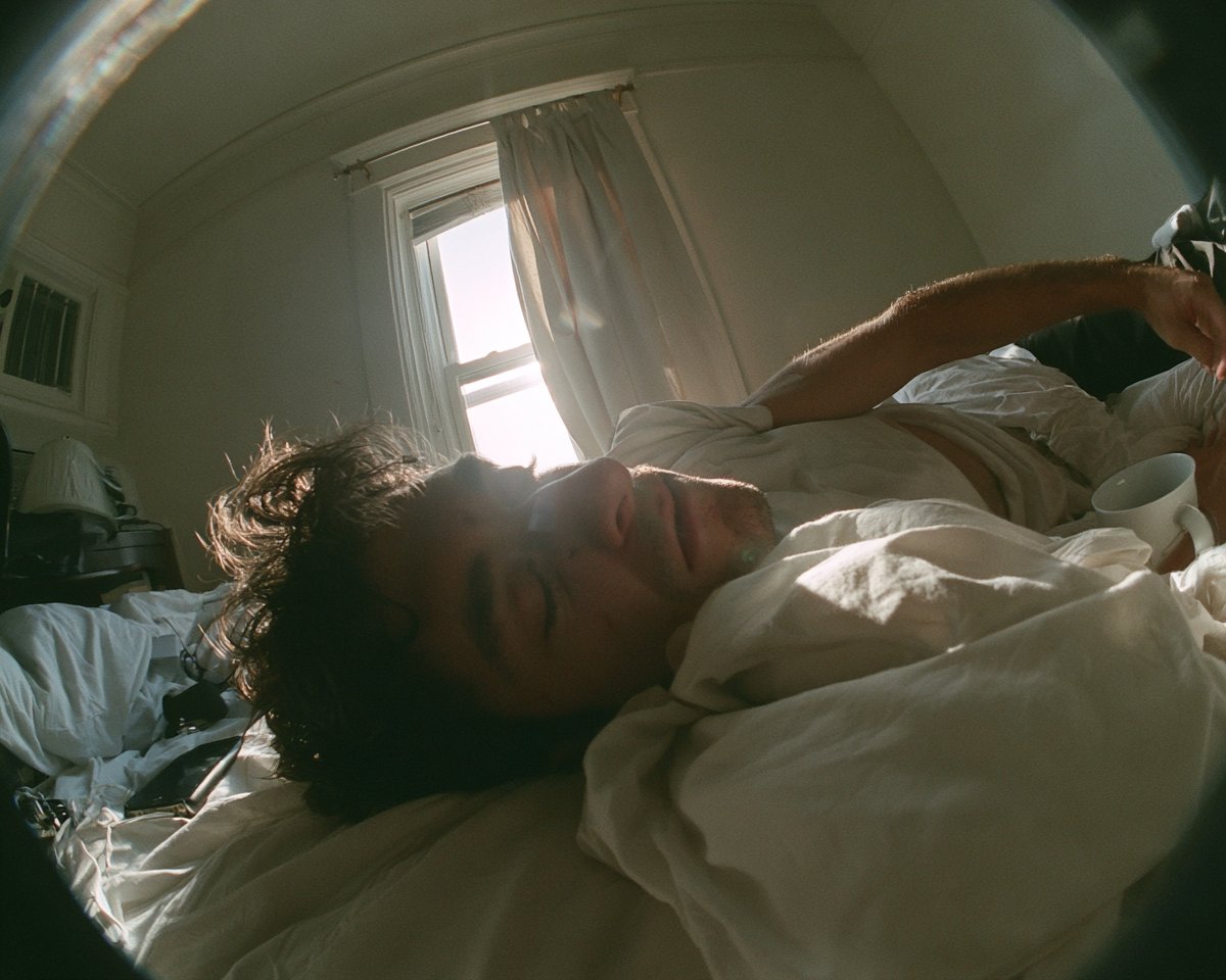 Candid fisheye action-camera photograph of a young adult man stretching in bed …