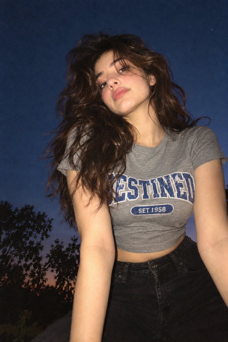 A low-angle, close-up photograph capturing a young woman with wavy brown hair o…